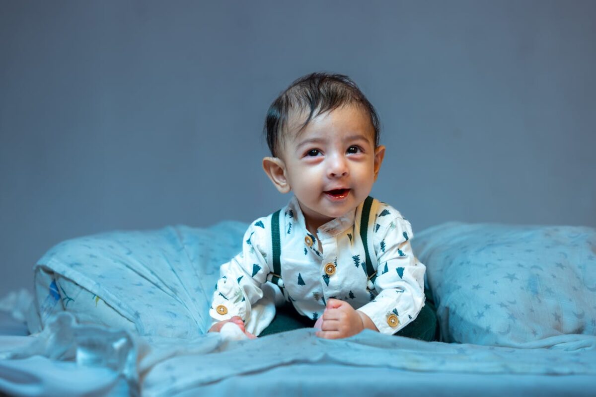 Charming baby in cute outfit sitting on a cozy bed surrounded by a soft blue blanket.