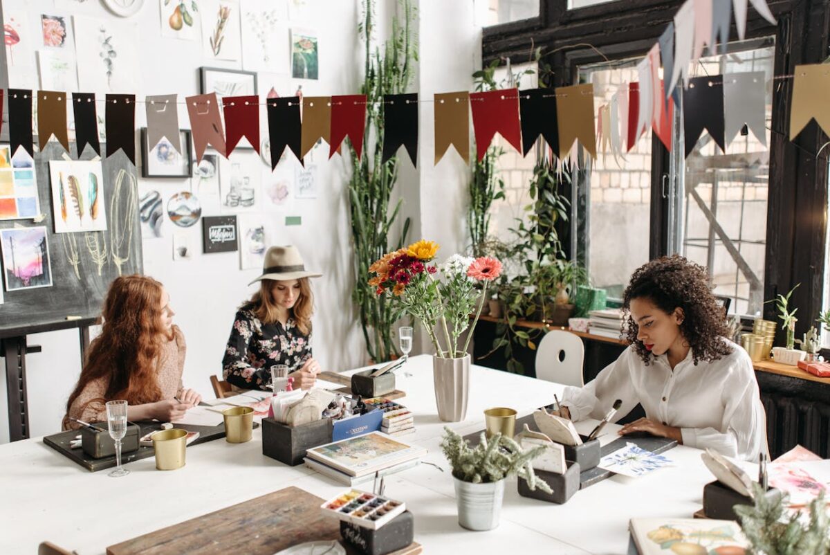 Three women engaged in a creative workshop, painting and drawing in a well-decorated studio space.